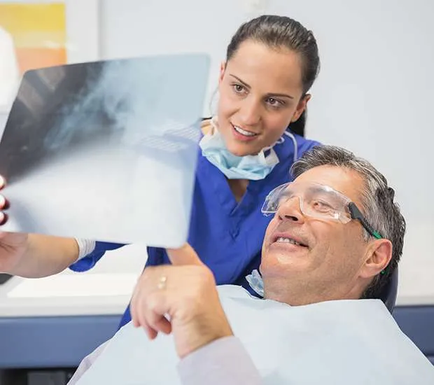 A dental assistant and a dentist hold up an x-ray while an older man sits back in the dental chair.