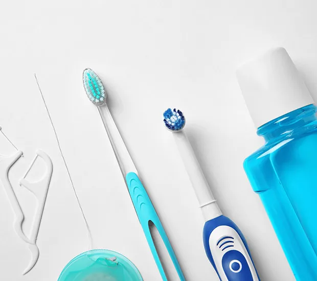 A toothbrush, an electric toothbrush, floss and a bottle of blue mouthwash laid out on a white surface.
