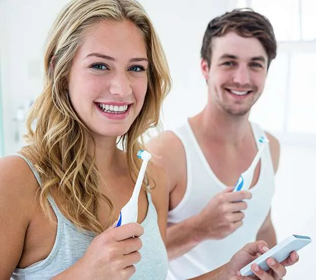 A smiling woman and man each holding a toothbrush.