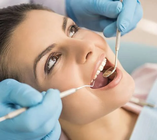 A dental hygienist examines a woman's gum line with a mirror and a probe.