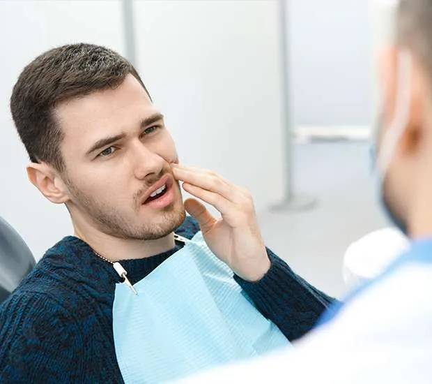A man in a dental bib touches his jaw while a dentist listens.