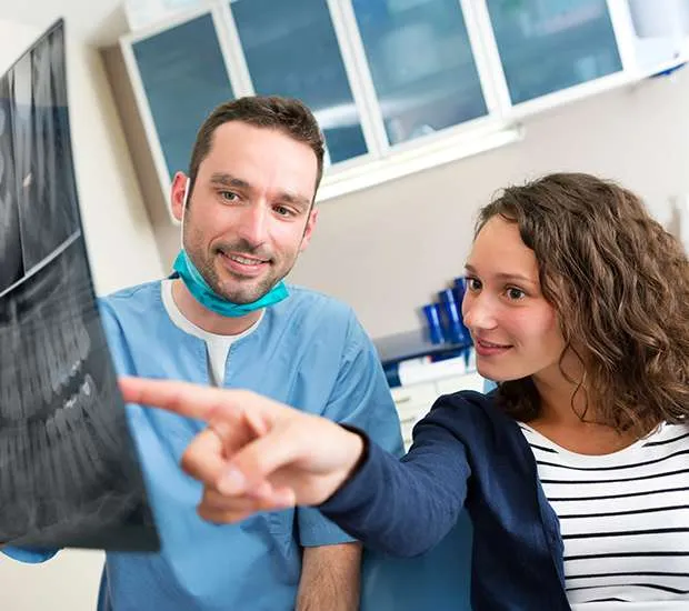 A dentist and a woman look at a dental x-ray together, the woman pointing at it.