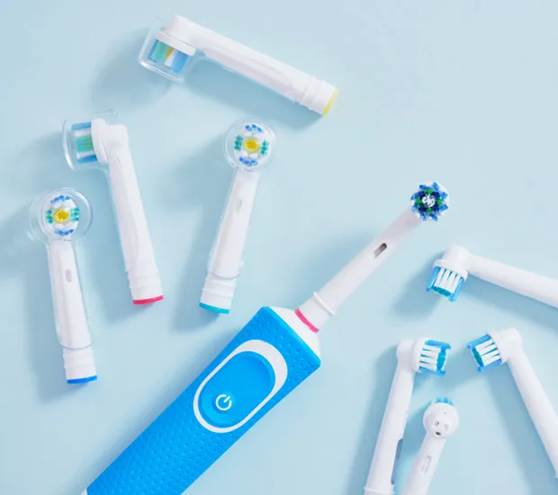A blue electric toothbrush and several replacement brush heads on a pale blue surface.