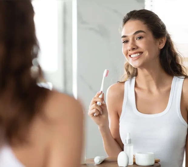 A smiling woman holds a toothbrush at a bathroom counter.