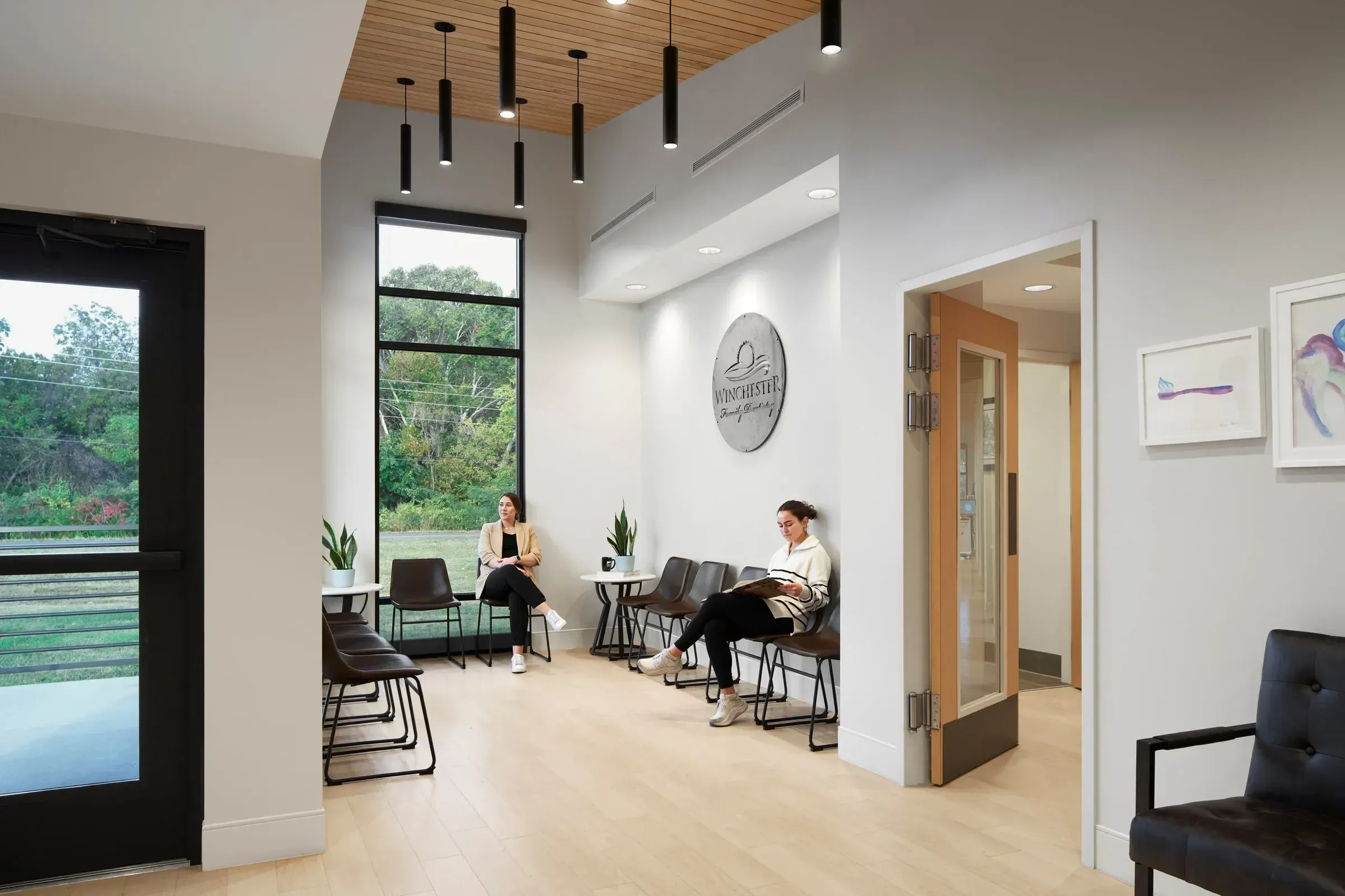 The waiting room at Winchester Family Dentistry: tall window, wood ceiling, the practice name on the wall and two patients seated.