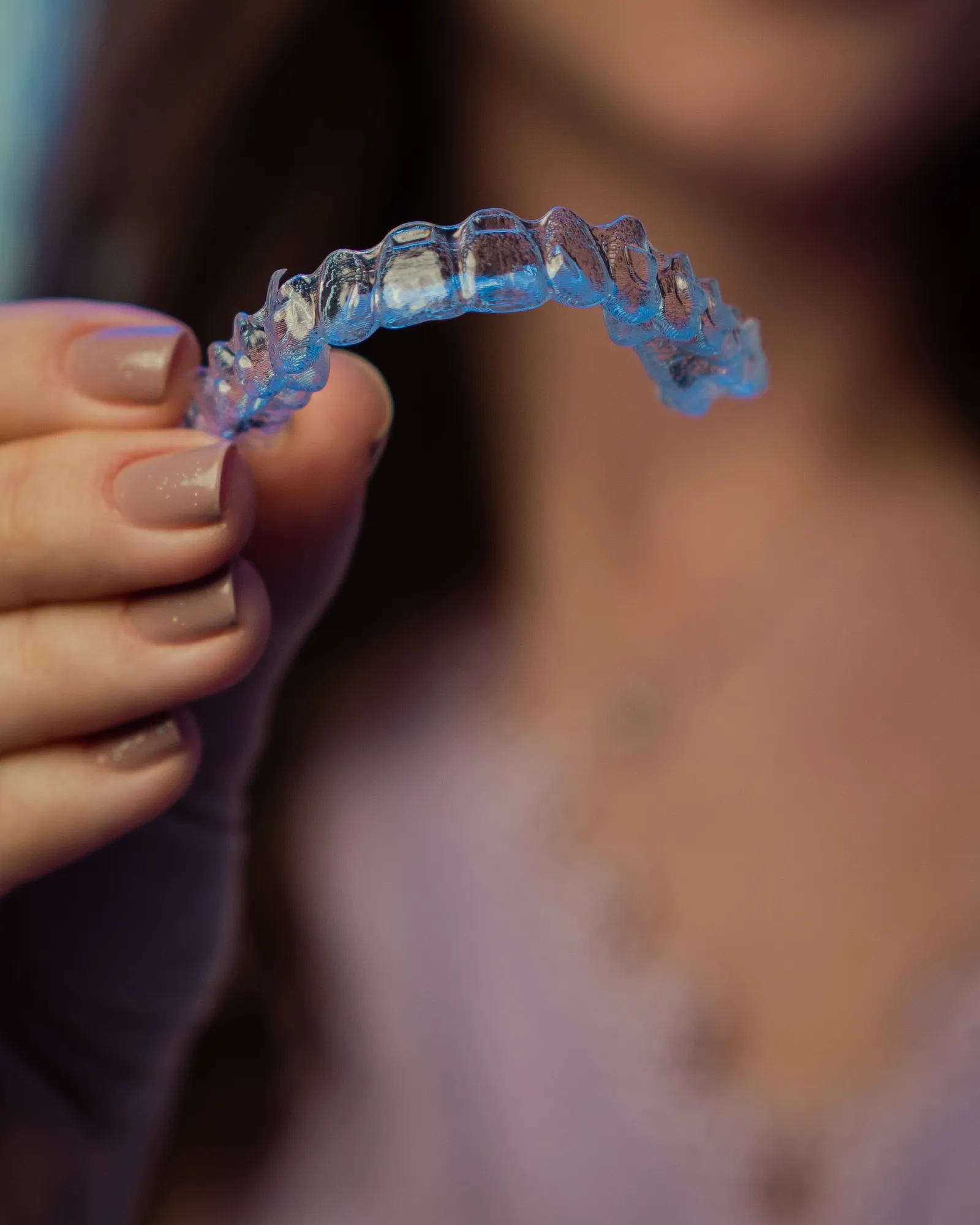 A clear aligner tray held up between finger and thumb.