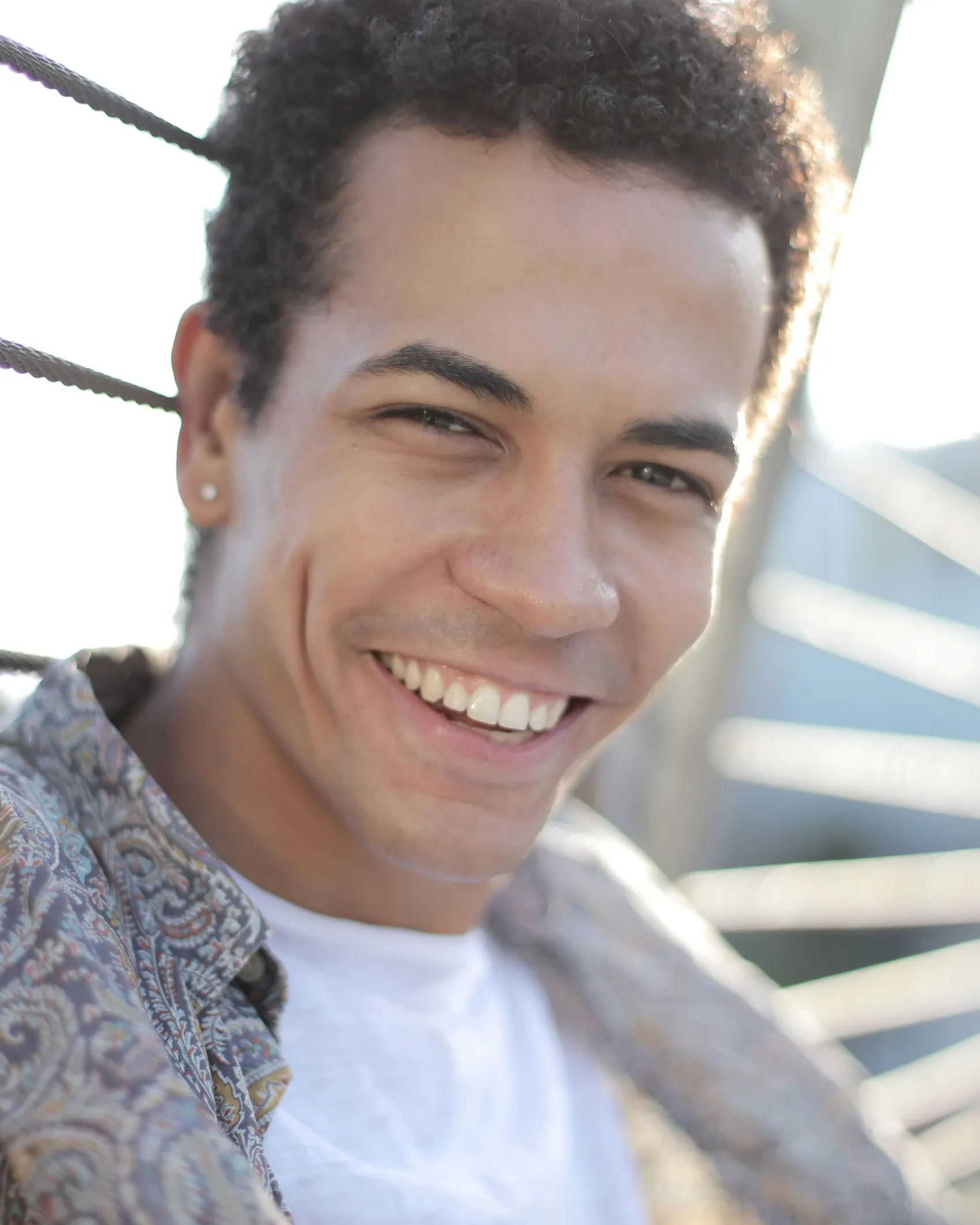 A young man smiling outdoors in bright sun.