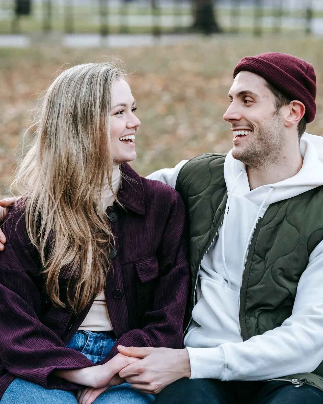 A young woman and a man laughing as they look at each other, seated close together on a park bench.