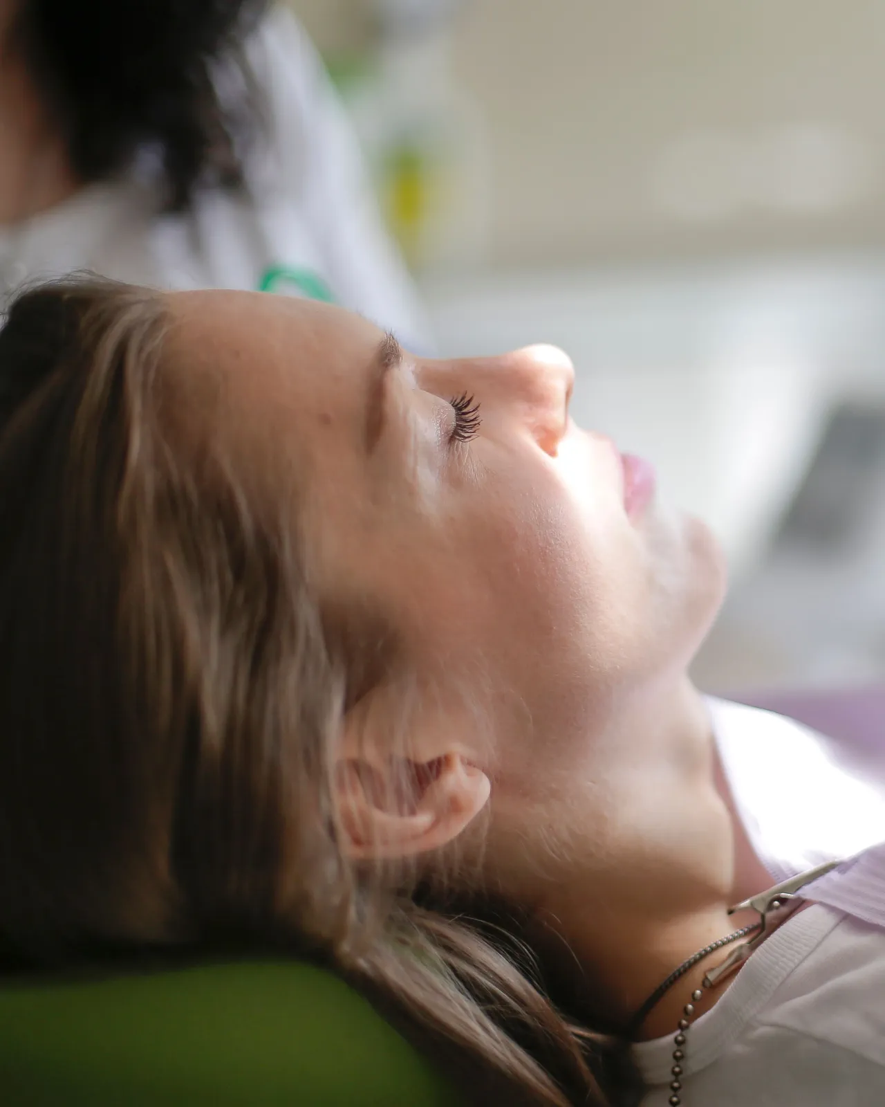 A young woman reclined in a dental chair with her eyes closed, light falling across her face.