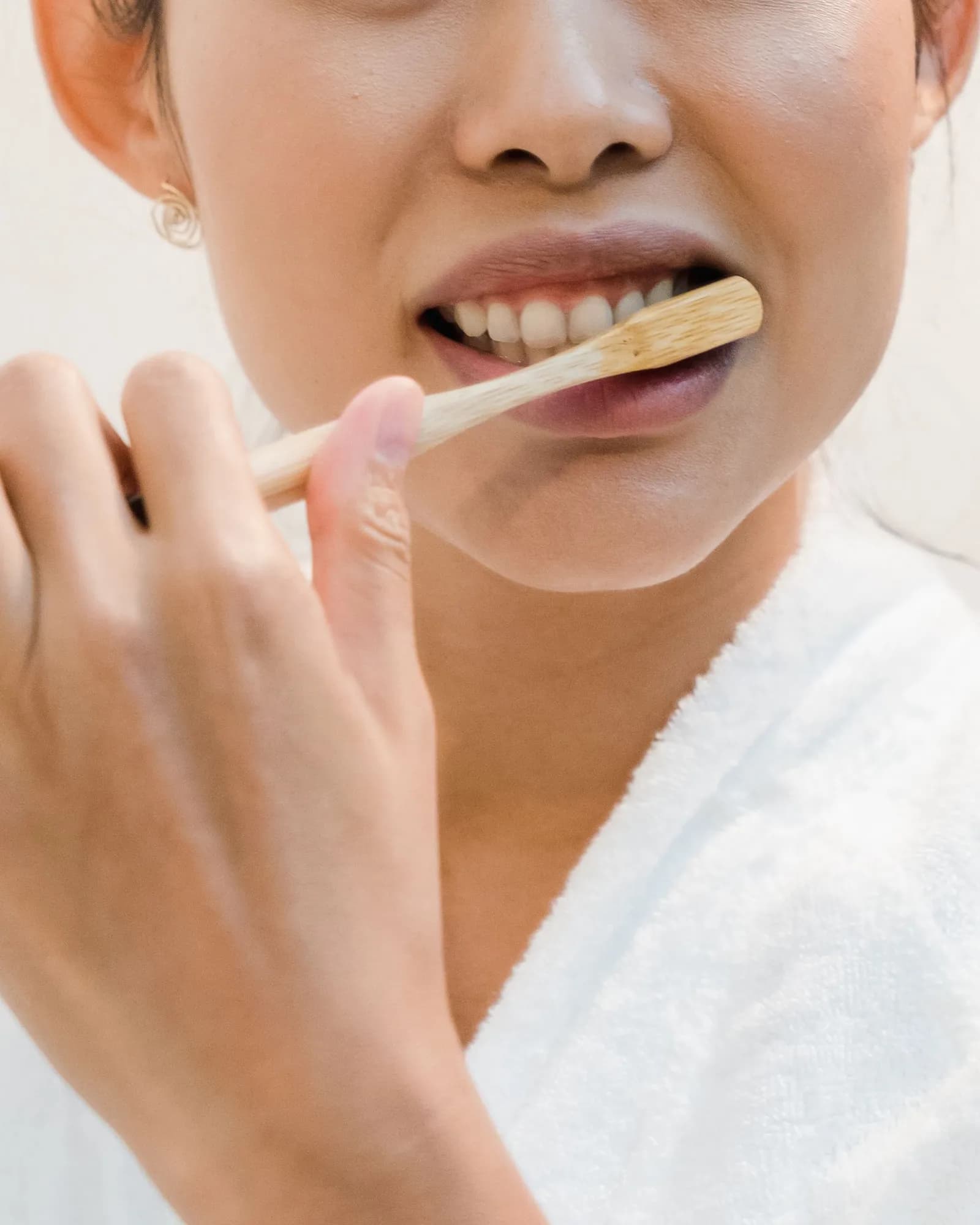 A woman in a white robe brushing her teeth with a bamboo toothbrush.
