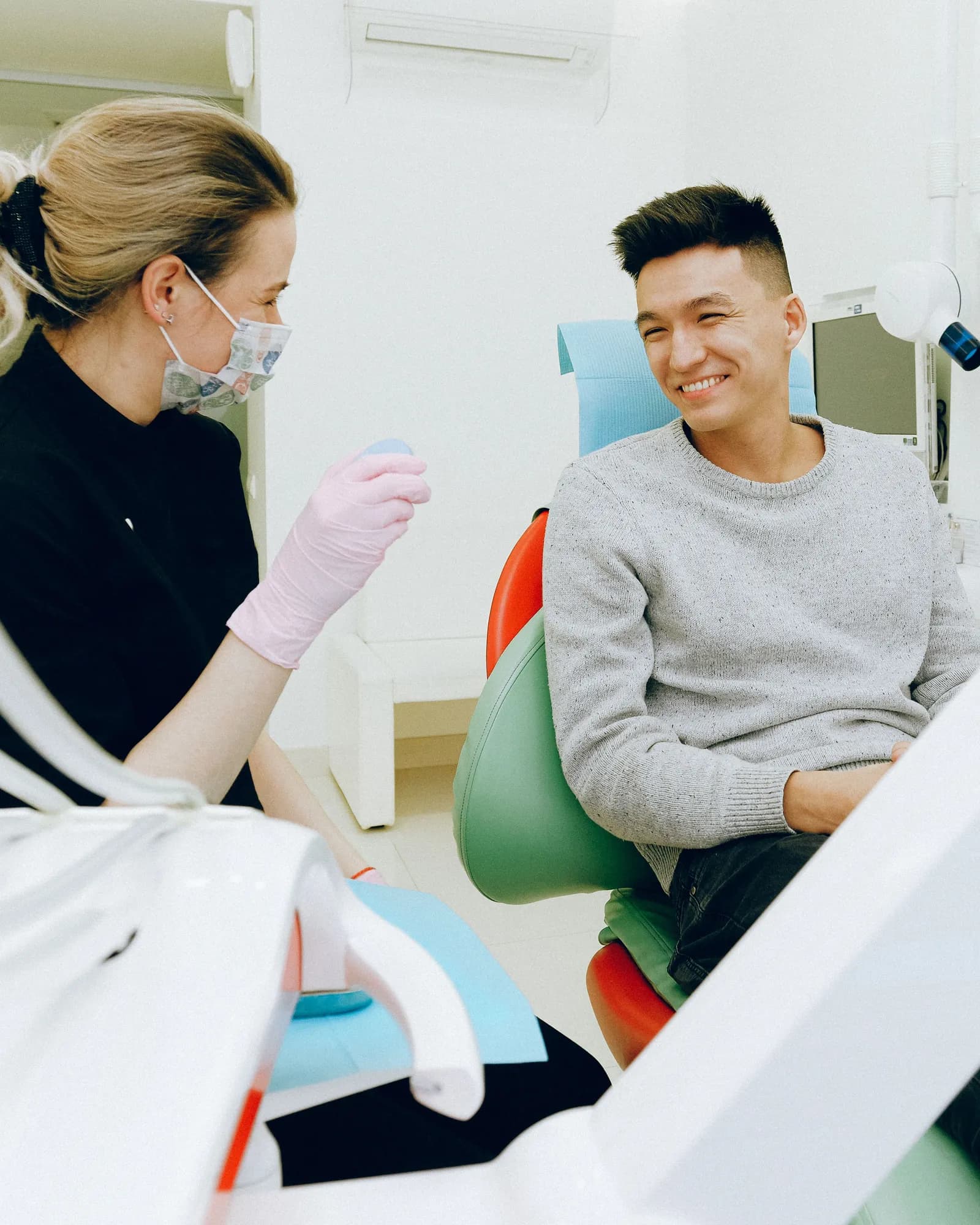 A dentist in a mask talking with a smiling man seated in a dental chair.