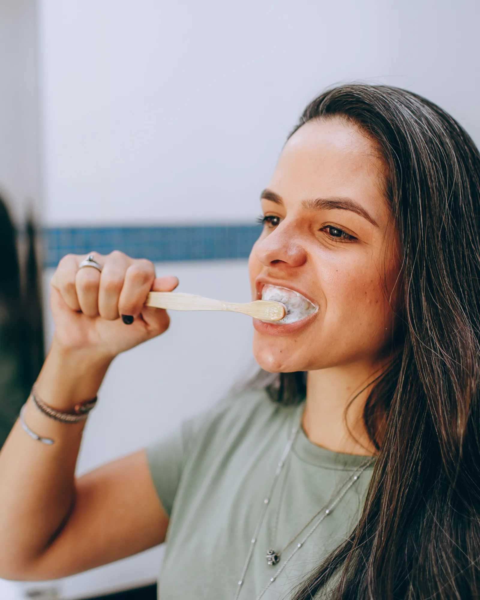 A woman brushing her teeth at a bathroom mirror, her reflection behind her.