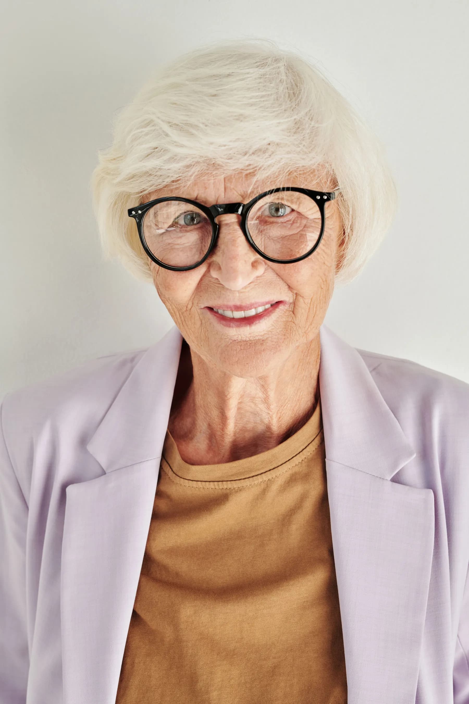 An older woman with short white hair and round dark glasses, smiling gently at the camera.