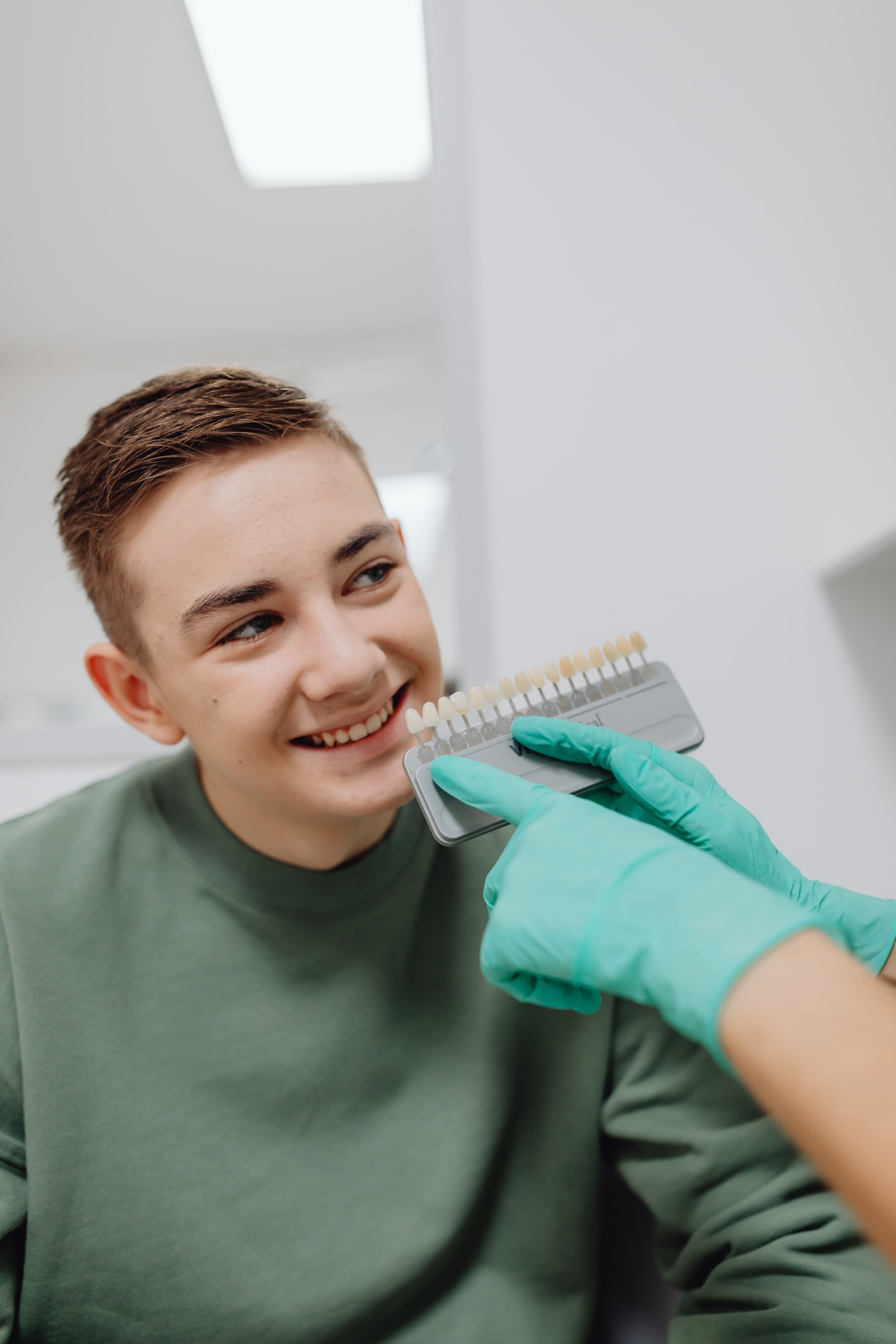 A dental shade guide held beside a patient's smile to match veneer color